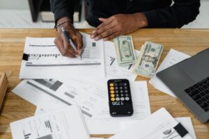 Man working on financial reports with calculator, money, and laptop on a desk. - Photo by Tima Miroshnichenko on Pexels
