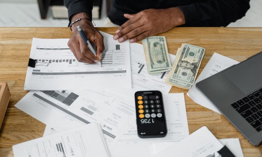 Man working on financial reports with calculator, money, and laptop on a desk. - Photo by Tima Miroshnichenko on Pexels